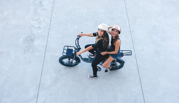 Two smiling girls roll together on a two -seater electric bike